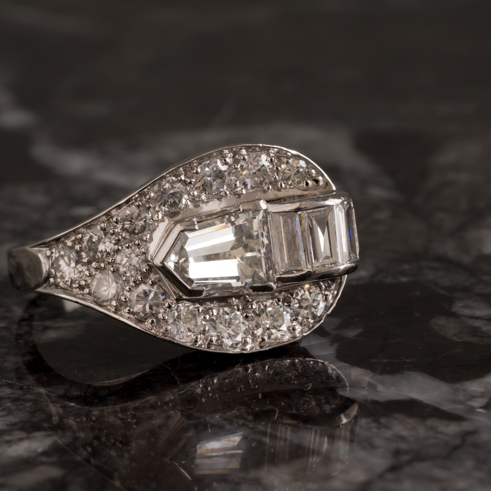 Platinum ring set with a bullet shaped diamond of estimated weight 0.70ct graded as colour G-H clarity VS to a curved feature set with three baguette cut diamonds and a surround of grain set diamonds on a plain polished band. Total Estimated Diamond Weight: 2.00ct Weight: 12.26grams Age: C1940 $14,500